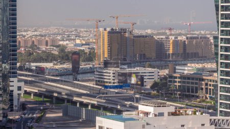 Foto de Sitio de construcción alrededor del canal de agua de Dubái con muchas grúas timelapse aéreo. Las casas y villas están detrás. Tráfico en el puente de la autopista por la mañana con largas sombras - Imagen libre de derechos