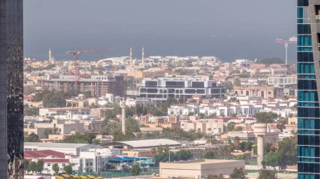 Foto de Nueva parte moderna con edificios de poca altura y villas creadas como calles de estilo europeo. Vista aérea del timelapse del distrito Dubai City Walk. Grúas de construcción sobre fondo con mezquitas - Imagen libre de derechos