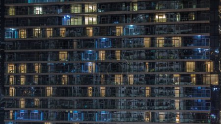 Photo for Tall blocks of flats with glowing windows located in residential district of city aerial timelapse. Evening light in rooms in towers and skyscrapers. Balconies with chairs and tables - Royalty Free Image