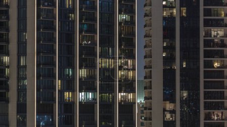 Photo for Evening light in rooms in towers and skyscrapers. Tall blocks of flats with glowing windows located in residential district of city aerial timelapse. - Royalty Free Image
