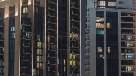 Téléchargez les photos : Grands blocs d'appartements avec fenêtres lumineuses situés dans le quartier résidentiel de la ville timelapse aérien. Lumière du soir dans des appartements dans des tours et des gratte-ciel - en image libre de droit