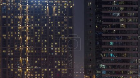 Téléchargez les photos : Grands blocs d'appartements avec de nombreuses fenêtres lumineuses situées dans le quartier résidentiel de la ville timelapse aérien. Lumière du soir dans les pièces des grandes tours et des gratte-ciel - en image libre de droit