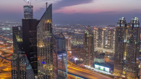 Téléchargez les photos : Bâtiments de grande hauteur sur Sheikh Zayed Road à Dubaï passage aérien du jour à la nuit timelapse, EAU. gratte-ciel dans le quartier financier international d'en haut. Maisons de promenade en ville et villas sur un fond - en image libre de droit