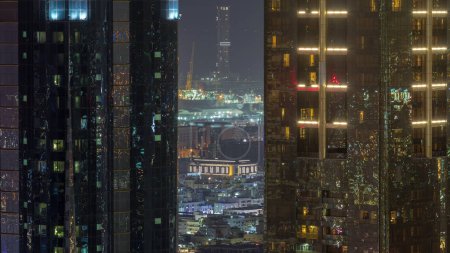 Téléchargez les photos : Vue aérienne entre deux gratte-ciel et des maisons d'appartements et villas dans la ville de Dubaï près du centre-ville timelapse de nuit. Grues éclairées du port maritime à distance. Émirats arabes unis - en image libre de droit