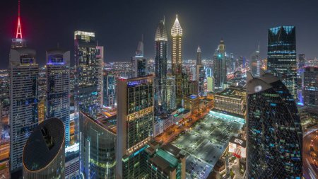 Foto de Vista del horizonte de los edificios de gran altura en Sheikh Zayed Road en Dubai timelapse noche aérea, Emiratos Árabes Unidos. Rascacielos iluminados y estacionamiento en el Centro Financiero Internacional desde arriba - Imagen libre de derechos