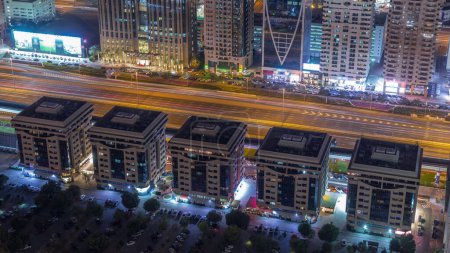 Téléchargez les photos : Bâtiments sur Sheikh Zayed Road à Dubaï timelapse de nuit aérienne, EAU. gratte-ciel dans le quartier financier international d'en haut. Circulation sur une autoroute et parking - en image libre de droit