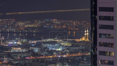 Foto de Vista aérea de casas de apartamentos y villas en la ciudad de Dubai cerca del timelapse del centro de la noche. Mezquita iluminada detrás de rascacielos. Emiratos Árabes Unidos - Imagen libre de derechos