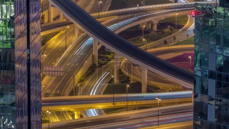 Téléchargez les photos : Vue aérienne d'en haut à un grand carrefour routier achalandé avec ligne de métro dans le centre-ville de Dubaï timelapse de nuit. Voitures conduisant directement dans les deux sens. Ponts et operpass éclairés - en image libre de droit