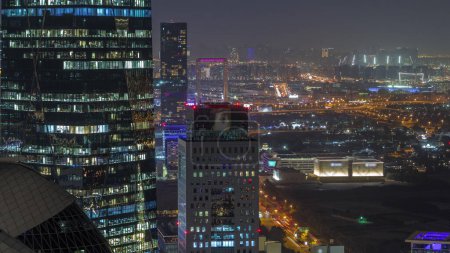 Foto de Vista aérea del tráfico en la calle Al Saada en el horario nocturno del distrito financiero en Dubai, Emiratos Árabes Unidos. Rascacielos iluminados y ventanas brillantes en torres de oficinas desde arriba. Deira sobre un fondo - Imagen libre de derechos