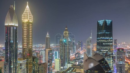 Foto de Vista panorámica de edificios de gran altura en Sheikh Zayed Road en Dubai timelapse noche aérea, Emiratos Árabes Unidos. Rascacielos iluminados en el Centro Financiero Internacional desde arriba - Imagen libre de derechos