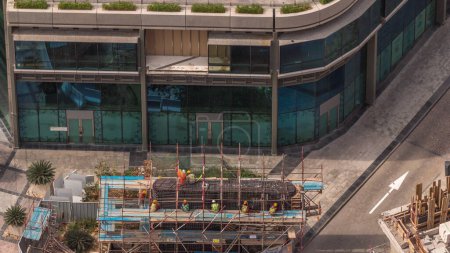 Foto de Muchos trabajadores en el sitio de construcción haciendo marco de metal de refuerzo para hormigón verter timelapse aéreo. Construcción de una nueva conexión puente entre rascacielos. Dubai - Imagen libre de derechos