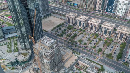 Foto de Sitio de construcción con grúas y edificios en Sheikh Zayed Road en Dubai, Emiratos Árabes Unidos. Rascacielos en el distrito financiero desde arriba con largas sombras en movimiento. Estacionamiento con muchos coches - Imagen libre de derechos