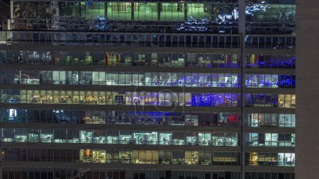 Photo for Frontal view of night facade of business tower building with a lot of windows with light timelapse. Life in every window. Aerial view of the glass facade of an office skyscraper. - Royalty Free Image