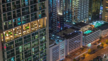 Téléchargez les photos : Piscine sur le toit au sommet d'un parking à plusieurs étages près de la route animée de Dubaï timelapse de nuit aérienne, Émirats arabes unis. Tours dans le Centre financier international d'en haut et fenêtres éclatantes - en image libre de droit