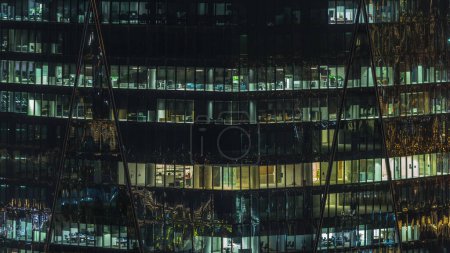 Photo for Frontal view of night facade of commercial tower building with a lot of panoramic windows with light timelapse. Life in every window. Aerial view of the glass facade of an office skyscraper. - Royalty Free Image