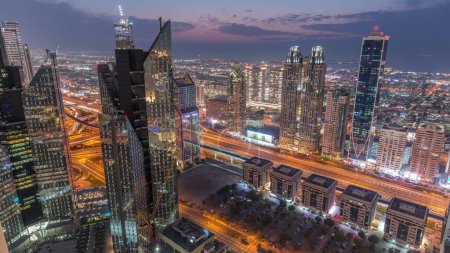 Téléchargez les photos : Bâtiments de grande hauteur sur Sheikh Zayed Road à Dubaï passage aérien du jour à la nuit timelapse, EAU. gratte-ciel dans le quartier financier international d'en haut. Maisons de promenade de la ville et circulation sur le fond - en image libre de droit