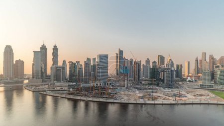Téléchargez les photos : Paysage urbain au coucher du soleil avec les gratte-ciel de Dubai Business Bay et le canal d'eau timelapse aérienne. Skyline moderne de tours résidentielles et de bureaux sur le front de mer. Immense chantier de construction sur la péninsule avec grues - en image libre de droit