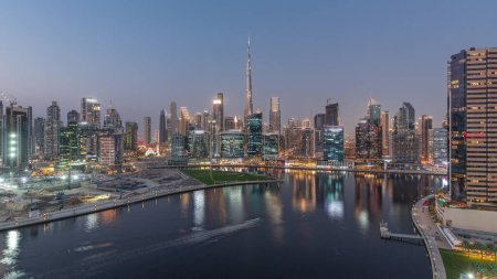Foto de Vista panorámica aérea de Dubai Business Bay y el centro de la ciudad con los diversos rascacielos y torres a lo largo de la costa en el canal de día a la noche timelapse transición. Lugar de construcción con grúas después del atardecer - Imagen libre de derechos