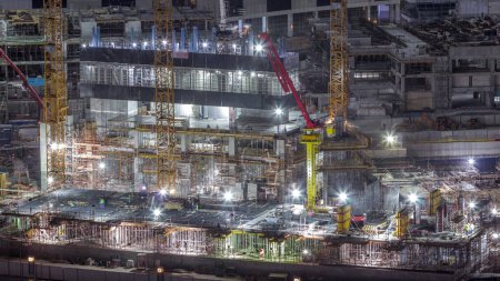 Photo for Large construction site with many working cranes and workers in uniform night timelapse. Top aerial view of big development of residential and office district in Business bay, Dubai - Royalty Free Image
