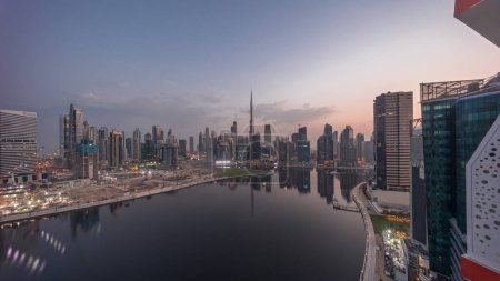 Photo for Aerial panorama of Dubai Business Bay and Downtown with the various skyscrapers and towers along waterfront on canal night to day transition timelapse. Construction site with cranes before sunrise - Royalty Free Image