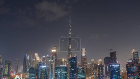 Photo for Aerial view to Dubai Business Bay and Downtown with the various skyscrapers and towers along waterfront on canal night timelapse. Construction site with cranes. Dark sky - Royalty Free Image