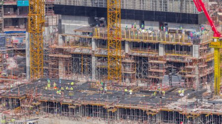 Photo for Large construction site with many working cranes timelapse. Workers in uniform and hard hats. Top aerial view of big development of residential and office district in Business bay, Dubai - Royalty Free Image