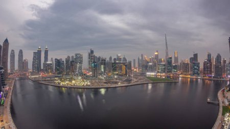 Téléchargez les photos : Vue aérienne vers Dubai Business Bay et le centre-ville avec les gratte-ciels panoramiques et les tours le long du front de mer sur le canal de jour à la période de transition nocturne. Site de construction avec grues après le coucher du soleil - en image libre de droit