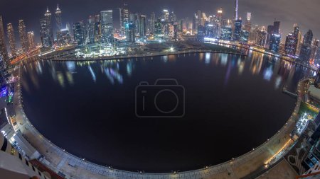 Photo for Aerial view to Dubai Business Bay and Downtown with the various skyscrapers and towers along waterfront on canal night timelapse. Boats and yacht floating on water. Construction site with cranes - Royalty Free Image