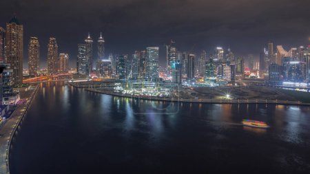 Photo for Cityscape panorama with illuminated skyscrapers of Dubai Business Bay and water canal aerial night timelapse. Modern skyline with residential and office towers on waterfront. Reflections in a river - Royalty Free Image