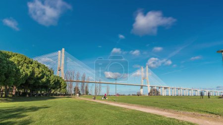 Téléchargez les photos : The Vasco da Gama Bridge timelapse hyperlapse with green lawn and trees. Cable-stayed longest bridge flanked by viaducts and rangeviews that spans Tagus River in Park of Nations in Lisbon, Portugal - en image libre de droit
