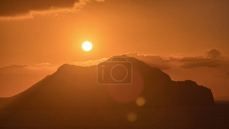 Foto de Puesta de sol en la isla de Amorgos timelapse aéreo desde arriba. Grecia tradicional - cielo naranja sobre montañas y colinas y mar turquesa, Cícladas - Imagen libre de derechos