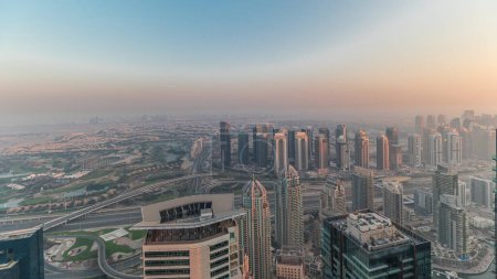 Foto de Panorama de Dubai Marina con rascacielos JLT y campo de golf timelapse durante la puesta del sol, Dubai, Emiratos Árabes Unidos. Vista aérea desde las torres superiores. skyline de la ciudad con tejados - Imagen libre de derechos