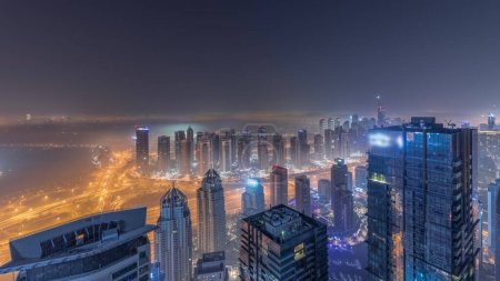 Foto de Panorama de Dubai Marina con rascacielos JLT y campo de golf durante toda la noche timelapse, Dubai, Emiratos Árabes Unidos. Vista aérea desde las torres superiores con niebla. Ciudad horizonte con luces apagadas - Imagen libre de derechos