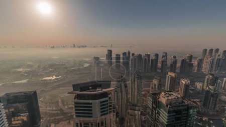 Photo for Panorama of Dubai Marina with JLT skyscrapers and golf course during sunrise timelapse, Dubai, United Arab Emirates. Aerial view from above towers foggy morning. City skyline with orange sky - Royalty Free Image