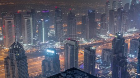 Téléchargez les photos : JLT gratte-ciel et port de plaisance de Dubaï près de Sheikh Zayed Road pendant toute la nuit intemporelle aérienne. Bâtiments résidentiels éclairés avec lumières éteintes - en image libre de droit