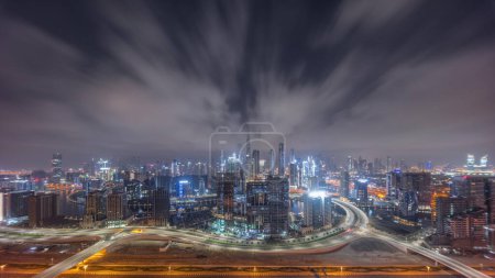 Téléchargez les photos : Skyline panoramique de Dubaï avec baie d'affaires et quartier du centre-ville toute la nuit. Vue aérienne de nombreux gratte-ciel modernes et la circulation achalandée sur la route al khail. Lune couchée et lumières éteintes. - en image libre de droit
