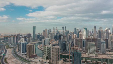 Foto de Skyline con la arquitectura moderna de Dubai torres de la bahía de negocios timelapse mañana. Vista panorámica aérea con canal y sitio de construcción durante el amanecer con cielo nublado - Imagen libre de derechos