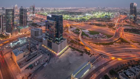 Téléchargez les photos : Un énorme carrefour autoroutier entre le quartier JLT et la ville médiatique croisée par Sheikh Zayed Road la nuit après le coucher du soleil. Terrain de golf près des tours et des gratte-ciel avec un trafic achalandé - en image libre de droit