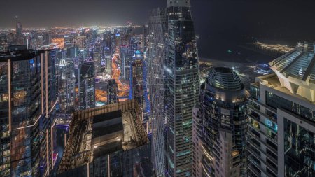 Foto de Panorama mostrando Dubai Marina con JLT y JBR distrito. Tráfico en carretera entre rascacielos noche aérea timelapse. Torres modernas iluminadas y obras de construcción - Imagen libre de derechos