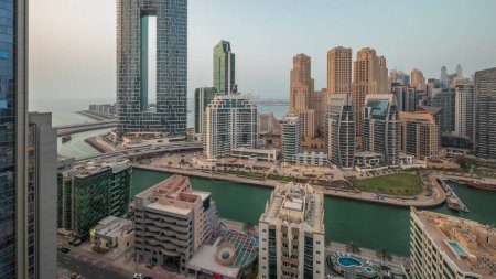 Téléchargez les photos : Panorama montrant Dubai Marina avec plusieurs bateaux et yachts garés dans le port et les gratte-ciel autour du canal timelapse aérien. Tours du quartier JBR sur fond - en image libre de droit