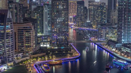 Photo for Dubai Marina with several boat and yachts parked in harbor and skyscrapers around canal aerial day to night transition timelapse. Towers along illuminated waterfront - Royalty Free Image