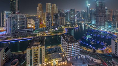 Téléchargez les photos : Marina de Dubaï avec des bateaux et des yachts garés dans le port et des gratte-ciel éclairés autour du canal timelapse panoramique aérienne pendant toute la nuit. Tours du quartier JBR sur fond - en image libre de droit
