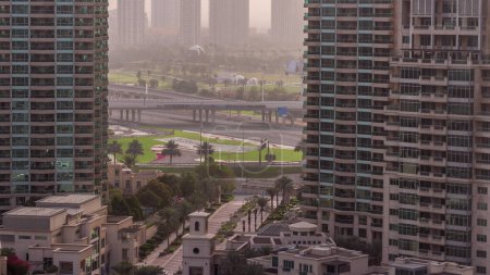 Téléchargez les photos : Vue aérienne du lever du soleil sur les tours dans le quartier des verts timelapse de la marina de Dubaï avec brouillard matinal. Gratte-ciels avec terrain de golf en face d'elle d'en haut. - en image libre de droit