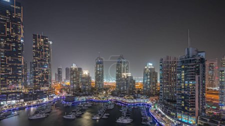 Téléchargez les photos : Panorama montrant les plus hauts gratte-ciels et yachts de la marina de Dubaï dans le timelapse de nuit aérienne du port. Vue sur les immeubles d'appartements, les hôtels et les immeubles de bureaux, développement résidentiel moderne des EAU - en image libre de droit