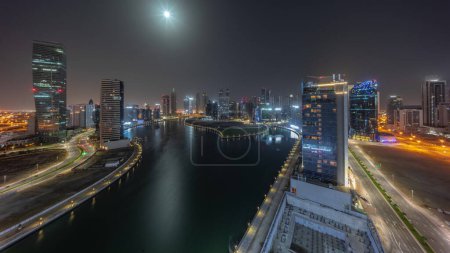 Téléchargez les photos : Paysage urbain de gratte-ciel à Dubai Business Bay avec canal d'eau aérien pendant la nuit timelapse avec la lune couchant vers le bas. Skyline moderne avec tours éclairées et lumières éteintes - en image libre de droit