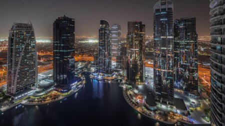 Téléchargez les photos : Panorama montrant de hauts bâtiments résidentiels dans le quartier JLT, timelapse de nuit aérienne, qui fait partie du quartier mixte du centre multi-commodités de Dubaï. Tours et gratte-ciel éclairés - en image libre de droit