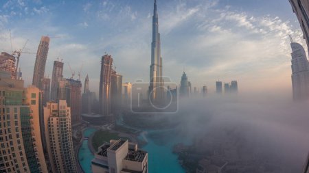 Téléchargez les photos : Vue aérienne de la ville de Dubaï tôt le matin pendant la nuit de brouillard à la transition quotidienne. Skyline futuriste de la ville avec des gratte-ciels et des tours au lever du soleil d'en haut - en image libre de droit