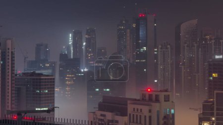 Photo for Dubai skyscrapers with illumination in business bay district during all night. Aerial view with fog from top of downtown in United Arab Emirates. Lights turning off - Royalty Free Image