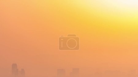 Foto de Salida del sol vista de cerca sobre el horizonte de Dubai por la mañana, vista aérea desde el puerto deportivo de Dubai. Gran sol en el cielo naranja se eleva sobre la niebla alrededor de los rascacielos. Emiratos Árabes Unidos - Imagen libre de derechos