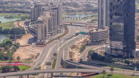 Foto de Enorme cruce de carreteras entre el distrito JLT y el puerto deportivo de Dubái intersecado por la antena Sheikh Zayed Road durante todo el día. Campo de golf cerca de torres y sombras moviéndose rápido - Imagen libre de derechos